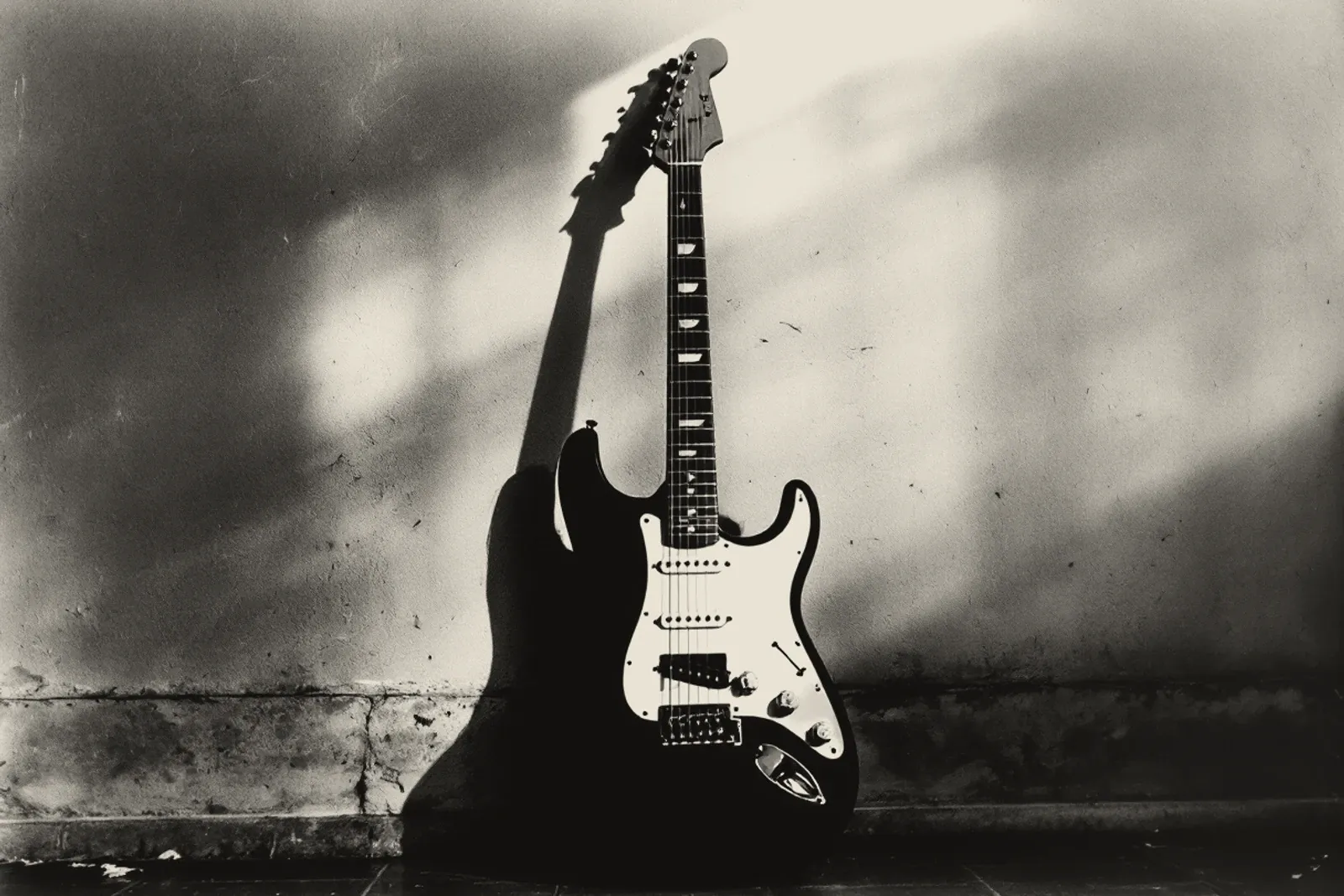 An electric guitar leaning against a bare wall in an empty room, raking light throwing its shadow across the plaster.